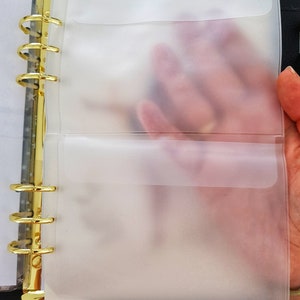 May include: A black binder with gold rings and two clear plastic pockets. The pockets are designed to hold papers or other items.