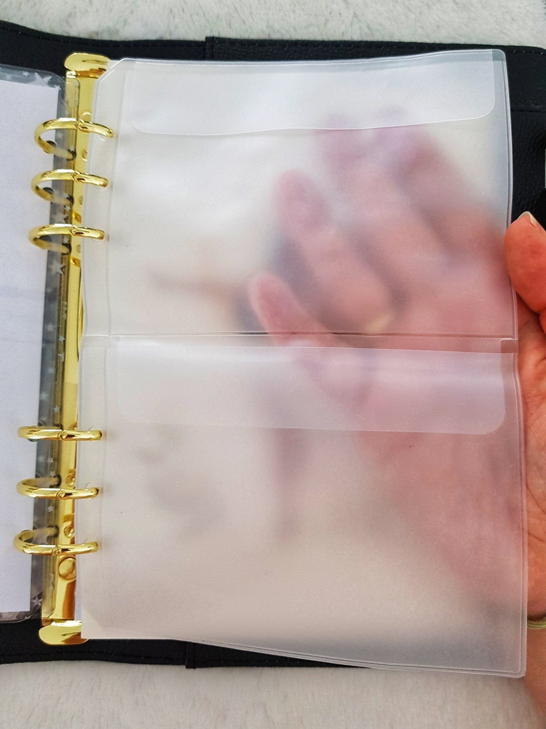 May include: A black binder with gold rings and two clear plastic pockets. The pockets are designed to hold papers or other items.