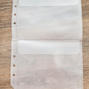 May include: Two clear plastic pockets with a flap closure and holes for a binder. The pockets are designed to hold papers or other small items.