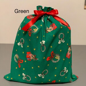 May include: Green fabric gift bag with a red satin ribbon drawstring. The bag is decorated with Christmas-themed illustrations, including wreaths, gifts, and stars. The word "Green" is printed at the top.