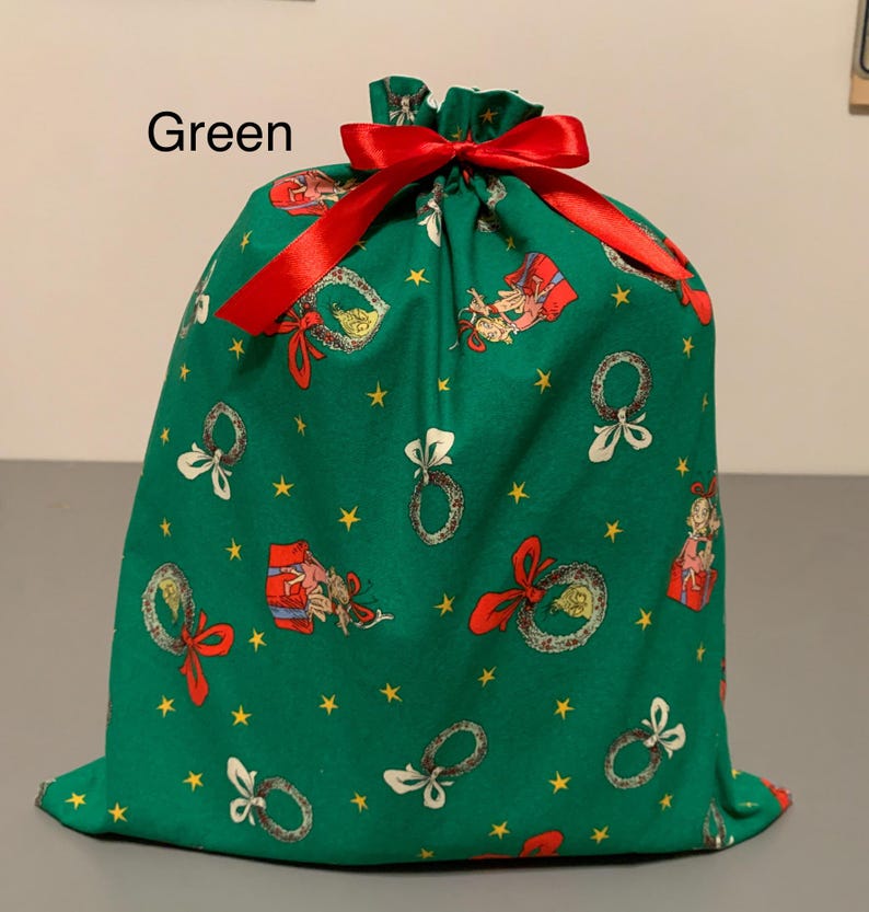 May include: Green fabric gift bag with a red satin ribbon drawstring. The bag is decorated with Christmas-themed illustrations, including wreaths, gifts, and stars. The word "Green" is printed at the top.