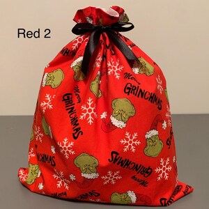 May include: Red Christmas gift bag with a black ribbon closure. The bag is covered in a pattern of the Grinch, snowflakes, and the words "Merry Grinchmas". The text "Red 2" is in the upper left corner.