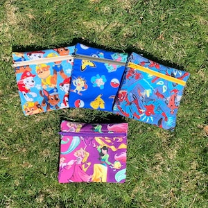 May include: Four zippered pouches with different colorful cartoon character designs. The pouches are made of fabric and have a zipper closure. The designs include Paw Patrol, Pokemon, Spiderman, and Disney Princesses.