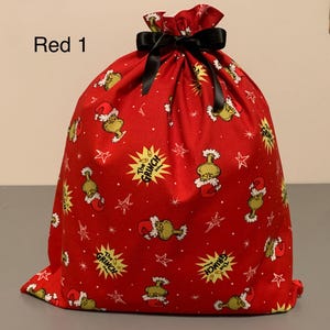 May include: Red drawstring gift bag with a black bow. The bag is covered in a pattern of the Grinch, stars, and text that says "The Grinch". The text "Red 1" is in the upper left corner.