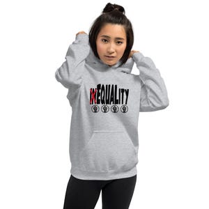 Op de afbeelding: Een lichtgrijze hoodie met het woord "INEQUALITY" in zwart en rood. Onder de tekst staan vier zwarte vuistsymbolen. De hoodie heeft een capuchon en een voorzak.