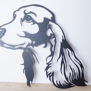 May include: A black metal silhouette of a dog's head with long, flowing ears. The silhouette is cut out of metal and has a matte finish.