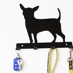 Könnte beinhalten: Schwarzer Schlüsselhalter aus Metall in Form einer Chihuahua-Silhouette mit drei Haken. Ein blauer Schlüsselanhänger, zwei Schlüssel und zwei Leinen hängen an den Haken.