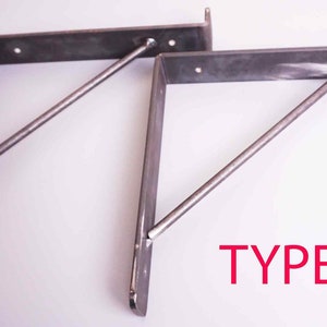 K&ouml;nnte beinhalten: Zwei Metall-Regalhalterungen mit einer diagonalen St&uuml;tzstange. Die Halterungen sind hellgrau und die St&uuml;tzstange ist dunkelgrau. Der Text "TYPE 2" ist in Rot unter den Halterungen gedruckt.