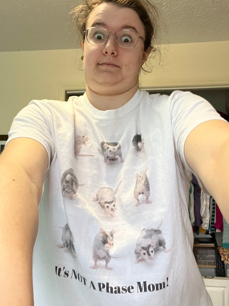 Pode incluir: Camiseta branca com um gr&aacute;fico de v&aacute;rios gamb&aacute;s em diferentes poses. O texto "It's Not A Phase Mom!" est&aacute; impresso na parte inferior da camiseta.
