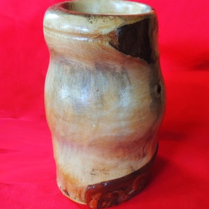 K&ouml;nnte beinhalten: Eine Holzvase mit nat&uuml;rlicher Holzmaserung. Die Vase hat eine hellbraune Farbe mit dunkleren braunen Akzenten. Die Vase besteht aus einem einzigen St&uuml;ck Holz und hat eine glatte, polierte Oberfl&auml;che.