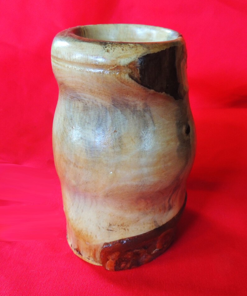 K&ouml;nnte beinhalten: Eine Holzvase mit nat&uuml;rlicher Holzmaserung. Die Vase hat eine hellbraune Farbe mit dunkleren braunen Akzenten. Die Vase besteht aus einem einzigen St&uuml;ck Holz und hat eine glatte, polierte Oberfl&auml;che.