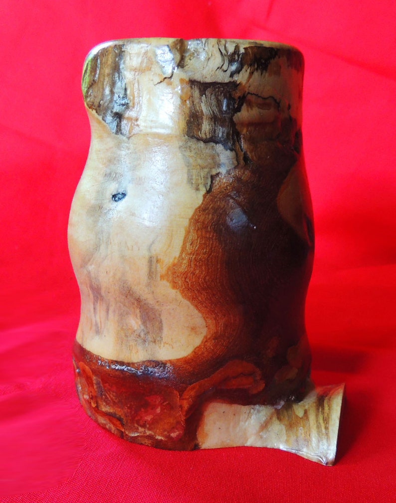 K&ouml;nnte beinhalten: Eine Holzvase mit einem nat&uuml;rlichen braunen und wei&szlig;en Holzmaserungsmuster. Die Vase hat eine einzigartige, unregelm&auml;&szlig;ige Form und einen Ausguss an der Seite.