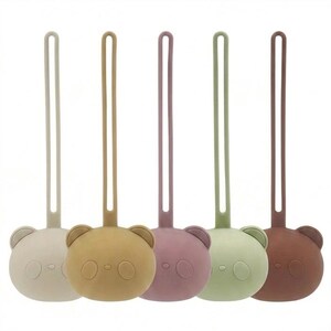 May include: Five silicone bear-shaped dummy clips in a row, each featuring a long, thin strap and a rounded bear face with two circular ears, a small nose, and two circular eyes. The colours are beige, mustard yellow, dusty rose, sage green, and brown.
