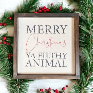 May include: A wooden framed sign with a white background and the text "Merry Christmas Ya Filthy Animal" in black and red lettering.