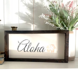 May include: A framed wooden sign with the word "Aloha" in black script and a pink hibiscus flower graphic.