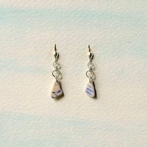 Puede incluir: Un par de pendientes de plata con colgantes de cerámica azul y blanca. Los colgantes tienen forma de triángulos irregulares con un patrón azul y blanco.