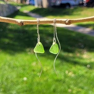 Puede incluir: Un par de pendientes de plata con forma de lágrima de vidrio de mar verde. Los pendientes están colgados de una rama.