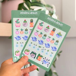 May include: Two rectangular sticker sheets titled as Pot Plant Cats Sticker Sheet by ashalind.draws. Each sheet features multiple small, colorful illustrations of cats integrated with various potted plants, cacti, and watering cans in pastel tones.