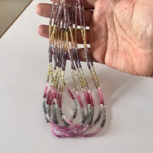 Puede incluir: Una hebra de cuentas de piedras preciosas multicolores, incluyendo rosa, morado, amarillo y gris, enhebradas en un alambre fino. Las cuentas están todas facetadas y tienen un ligero brillo.