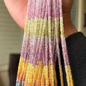 May include: A multi-strand beaded necklace with a gradient of colours. The beads transition from pink to yellow, orange, and blue. The necklace is held in a hand, showcasing the vibrant colour palette and intricate design.