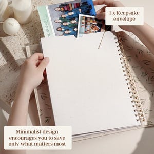 May include: A spiral-bound journal with a cream-colored cover and pages. The journal is open, with a photo being placed inside a keepsake envelope. The text "Minimalist design encourages you to save only what matters most" is visible.