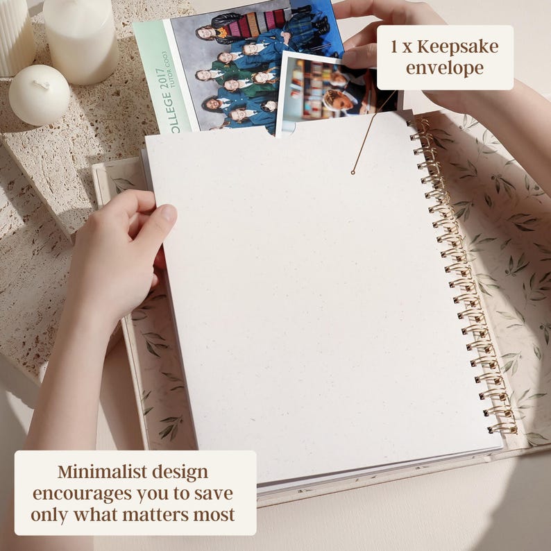 May include: A spiral-bound journal with a cream-colored cover and pages. The journal is open, with a photo being placed inside a keepsake envelope. The text "Minimalist design encourages you to save only what matters most" is visible.