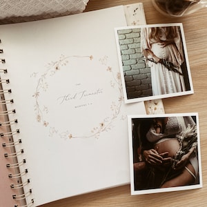 May include: A white journal with a gold spiral binding. The cover features a watercolor illustration of a floral wreath with the text "The Third Trimester Months 7-9". Two black and white photos of pregnant women are attached to the journal.