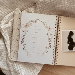 May include: A floral-themed journal with a gold spiral binding. The journal has a page with prompts for recording memories of the day a baby was born. The page includes prompts for the weather, the leader of the country, a top news story, the cost of milk, and a loaf of bread.