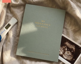 May include: A sage green "My Pregnancy Journal" notebook with gold lettering and the text "A Journey of Love & Growth." A pregnancy test and ultrasound image are also present.