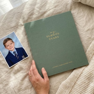 May include: A sage green memory book with the gold embossed text "MY SCHOOL YEARS" and "A SCHOOL YEARS MEMORY BOOK" on the cover, accompanied by a square photograph of a child wearing a blue blazer, white shirt, and striped tie.
