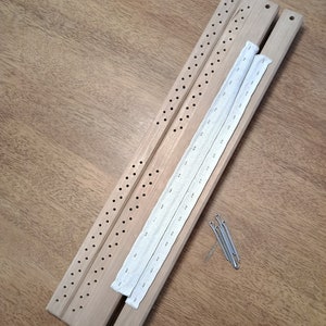 May include: Three wooden loom pieces with holes for weaving, a white elastic band, and five silver safety pins.