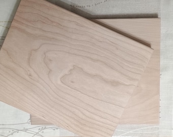 May include: Two wooden cutting boards, one on top of the other. The top board is larger and has a light wood grain pattern. The bottom board is smaller and has a darker wood grain pattern.