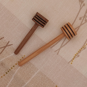 May include: Two wooden honey dippers, one with a light brown handle and a dark brown head, and the other with a light brown handle and a light brown head.