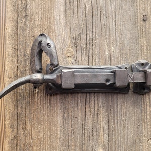 Puede incluir: Un pestillo de puerta de metal negro con un diseño de cabeza de caballo. El pestillo está montado en una puerta de madera.