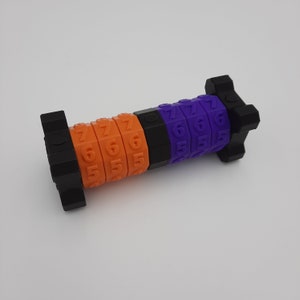 Puede incluir: Una cerradura de combinación de color morado y naranja con los números 5, 6 y 7. La cerradura está hecha de plástico y tiene una base negra.