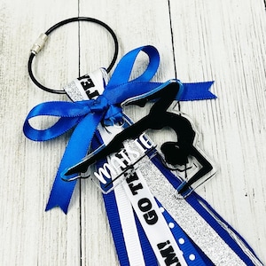 May include: A blue and silver cheer bow with a clear acrylic charm featuring a gymnast silhouette and the word "MARIS" on it. The charm is attached to a silver key ring.