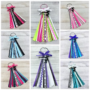 May include: Nine different hair ties with ribbons and a gymnast silhouette charm. The ribbons are in various colors and patterns, including black, white, pink, blue, green, purple, and teal. The charms are black and white. The hair ties are all tied with a bow.