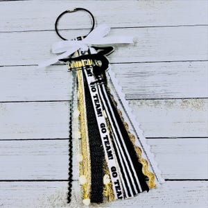 May include: Black and white cheer bow with gold glitter and white pom poms. The bow has a black and white striped ribbon with the text "GO TEAM! GO TEAM! GO TEAM!" printed on it.