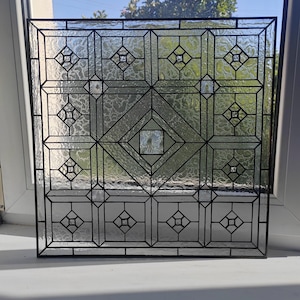 May include: A square stained glass panel featuring a geometric grid pattern with black lead lines. The design includes clear textured glass panes and small central diamond accents, with a larger central diamond motif framed by clear glass.