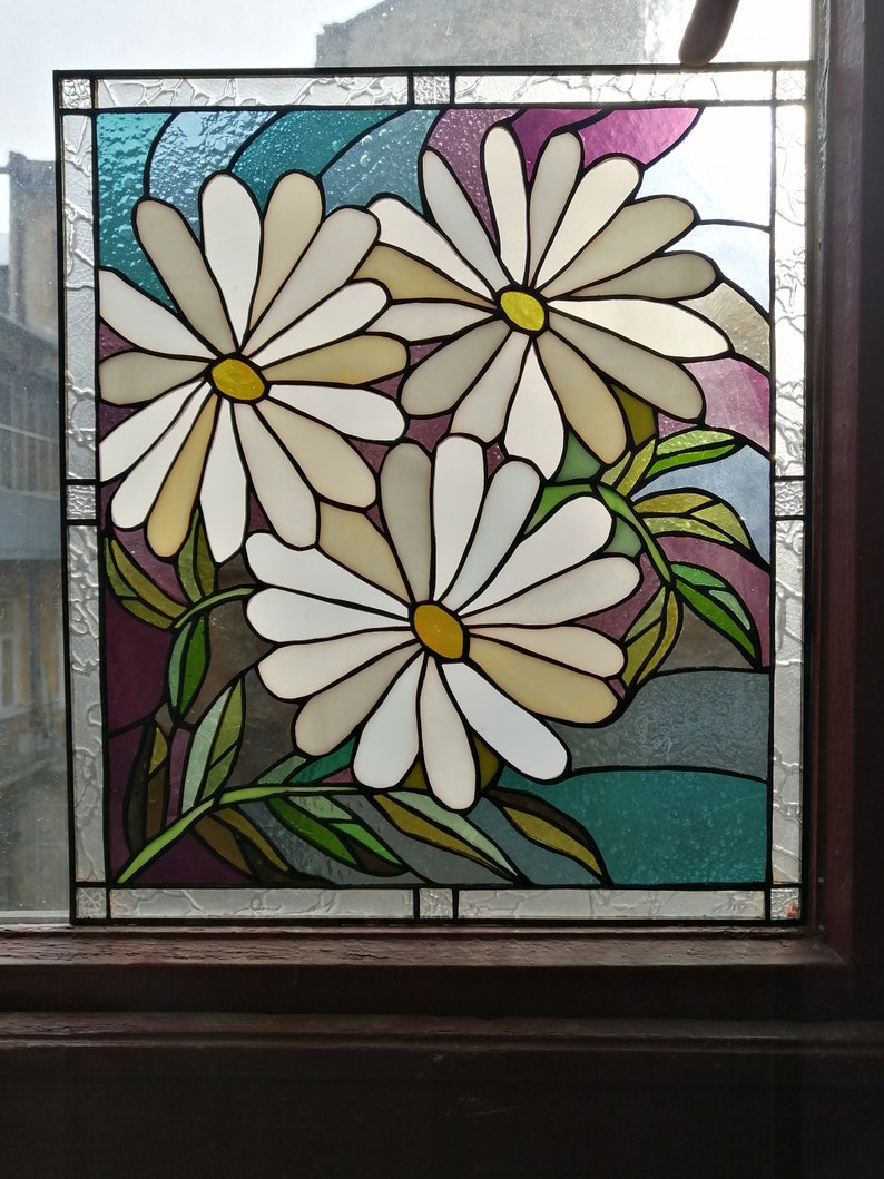 May include: A stained glass window featuring three white daisies with yellow centers, set against a background of purple, blue, and green.