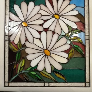 May include: A stained glass window featuring three white daisies with yellow centers. The daisies are set against a background of green, brown, and blue glass.