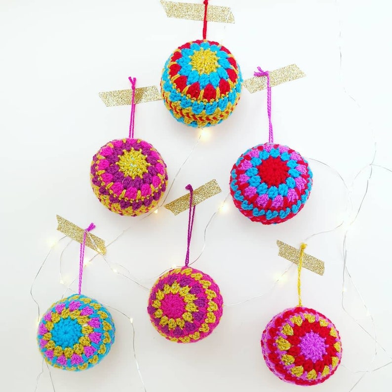May include: Six crocheted Christmas ornaments in various colors, including red, pink, yellow, blue, and green. Each ornament features a circular pattern with a central yellow circle.