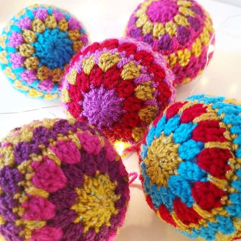May include: Five crocheted ornaments in various colors, including red, blue, purple, and gold. The ornaments are all round and have a textured surface.