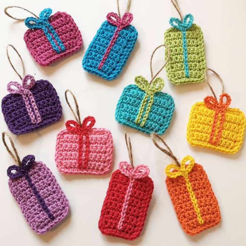 May include: Ten crocheted gift ornaments in various colors, including pink, purple, blue, green, yellow, and orange. Each ornament is shaped like a gift box with a bow on top.