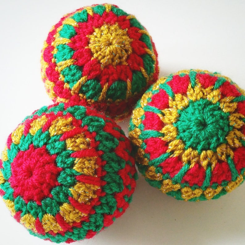 May include: Three crocheted ornaments in red, green, and gold. Each ornament features a circular pattern with a central flower design.