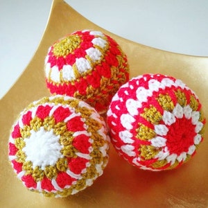 May include: Three crocheted Christmas ornaments in red, white, and gold. The ornaments are round and have a textured surface.