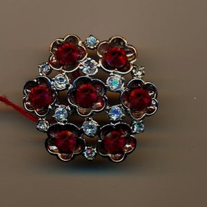 May include: A silver-toned brooch featuring a cluster of red and clear rhinestones in a flower design.