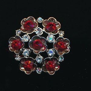 May include: A silver-toned brooch with a cluster of red and clear rhinestones in a flower shape.