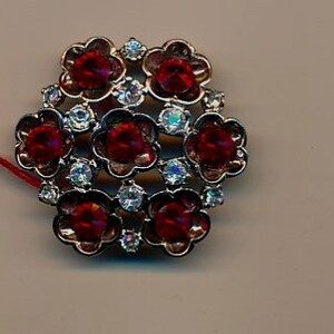 May include: A silver-toned brooch featuring a cluster of red and clear rhinestones in a flower design.