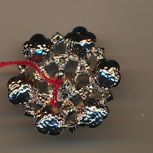 May include: A silver-toned metal embellishment with a red thread attached. The embellishment is shaped like a flower with a circular centre and six petals. Each petal has a raised, round bead at the end.